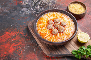Horizontal view of tasty meatballs soup with noodles on board lemon wooden pasta a bunch of greens on dark table