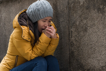 dramatic lifestyle portrait of young attractive sad and depressed Korean woman in winter hat sitting outdoors on street corner staircase suffering depression problem crying