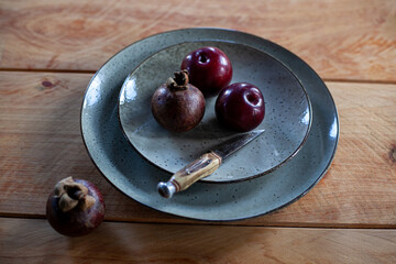 Whole purple plums and mangosteens and knife on ceramic plate on wooden table