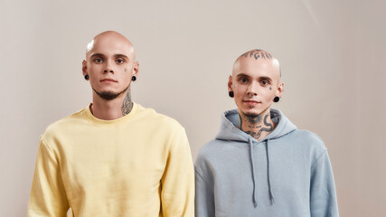 Portrait of young caucasian twin brothers with tattoos and piercings looking at camera while posing...