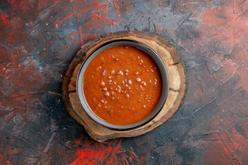 Overhead view of tomato soup in a blue bowl on a brown wooden tray on mixed color table