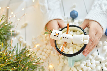 Girl holding cup of hot drink with marshmallow snowman at wooden table, top view. Bokeh effect. Happy New Year