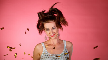 Portrait of Happy Brunette Woman with Falling Gold Confetti in the Air. Party or New Year Celebration. Pink Background.