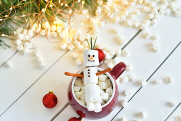 Funny marshmallow snowman in red cup of hot drink on light wooden table, flat lay. Space for text