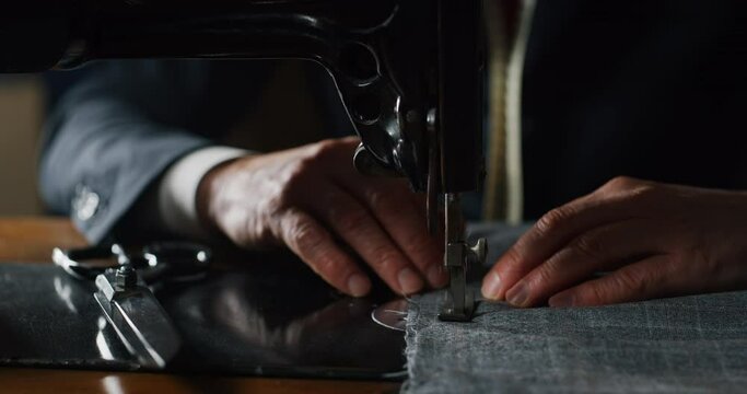 Cinematic macro shot of experienced tailor is sewing custom handmade high quality apparel in ancient luxury traditional tailoring atelier. Concept of industry, handmade, couturier and tradition.
