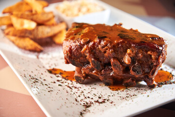 Closeup of pork ribs grilled with BBQ sauce and caramelized in honey. Tasty snack to beer on a wooden Board for filing on dark concrete background