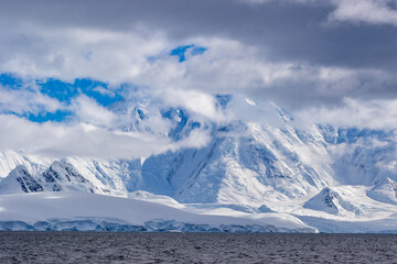 Snow-capped large mountains in Antarctica covered with gray clouds.