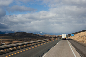 A picturesque highway along which cars and trucks drive among the mountains, slightly covered with snow, on a bright sunny autumn day. Oregon Scenic Hwy, OR, USA, 12-15-2019