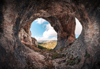 Panoramic of a large cave with two entrances. Interior of a cavern with a stone arch at the entrance. Cueva de los Arcos, Spain. Ancient ancestral cave in the mountain shows us a beautiful landscape