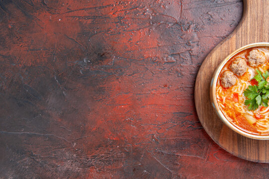 Half shot of tomato meatballs soup with noodles in a brown bowl on the right side of dark background stock photo