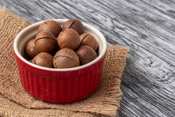 Whole macadamia nuts in red bowl on black wooden table.