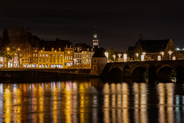 Fototapeta na wymiar Maastricht, Netherlands 12-11-2020 illuminated skyline with christmas decorations of downtown Maastricht and the old bridge with arches and reflections in the river Meuse