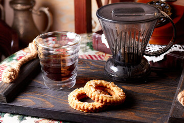 Close up of glass jug with alternatively brewed coffee, coffee brewing gadgets for drip coffee and glass of coffee, two cookies on wooden tray in cafe