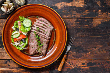 Grilled beef meat chop round steak on a plate with salad.  Dark wooden background. Top view. Copy space