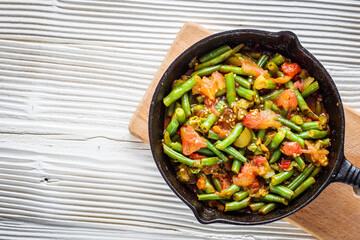 stewed green beans in a cast iron skillet on a white wooden rustic background