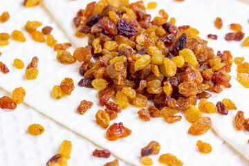 Brown raisins (dried yellow grape) on light textile background.