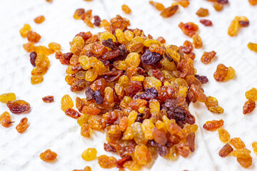 Brown raisins (dried yellow grape) on light textile background.