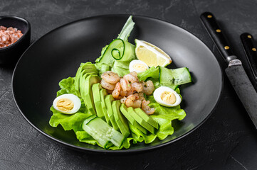 Fresh seafood salad with grilled shrimps prawns, egg, avocado and cucumber in a plate. Black background. top view