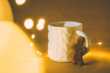 Unique ceramic tea cup with knit pattern with a gingerbread man cookie with warm Christmas lights and bokeh defocused effect