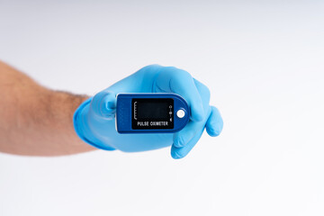 Pulse oximeter on a white background. A hand in a medical glove holds a device for health diagnostics