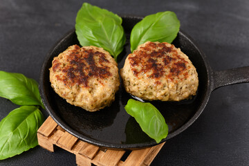 Fried meatball in a frying pan on a woodenpalet trivet, with basil leaves.
