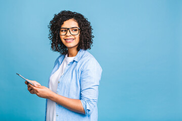 Portrait of young american student girl with curly african hair holding digital tablet and smiling standing over isolated blue background with copy space for text, logo or advertising.
