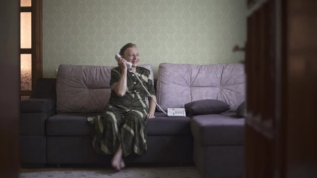 Grandmother is excited to hear someone on the phone and talks cheerfully. Old woman pleasantly talks on the wire phone. High quality FullHD footage