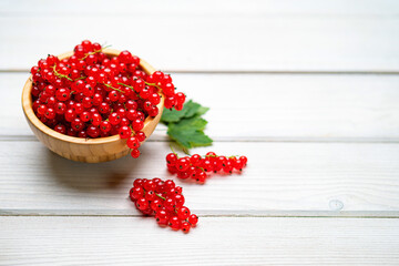 Fresh ripe red currant berries (Ribes rubrum) with leaves in bowl on white wooden table. Healthy organic food, summer vitamins, BIO viands, natural background. Copy space for advertising text message