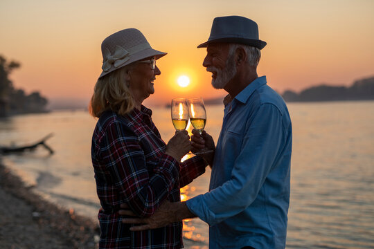 The happy senior couple is drinking wine and enjoying the sunset on the river.	