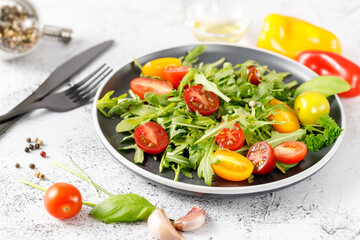 Vegetarian fresh arugula salad with cherry tomatoes, olive oil and spices on plate.