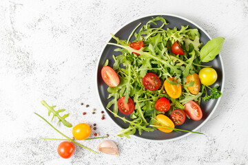 Vegetarian fresh arugula salad with cherry tomatoes, olive oil and spices on plate. Top view