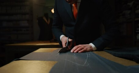 Cinematic macro shot of experienced tailor is cutting with scissors fine quality fabric for creation custom haute couture apparel in tailoring atelier. Concept of handmade, couturier and tradition.