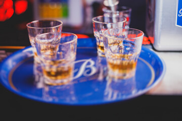 Beautiful row of different colored alcohol cocktails on a party, whiskey, scotch whisky, and others, glasses on a bar counter, bar stand, with bartender in the background