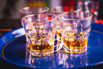Beautiful row of different colored alcohol cocktails on a party, whiskey, scotch whisky, and others, glasses on a bar counter, bar stand, with bartender in the background