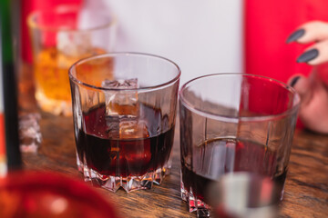 Beautiful row of different colored alcohol cocktails on a party, whiskey, scotch whisky, and others, glasses on a bar counter, bar stand, with bartender in the background