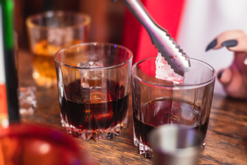 Beautiful row of different colored alcohol cocktails on a party, whiskey, scotch whisky, and others, glasses on a bar counter, bar stand, with bartender in the background