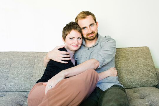 Couple looking at camera and embracing on sofa