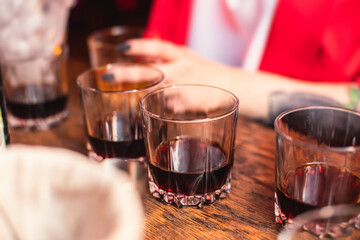 Beautiful row of different colored alcohol cocktails on a party, whiskey, scotch whisky, and others, glasses on a bar counter, bar stand, with bartender in the background