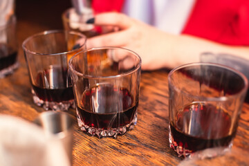Beautiful row of different colored alcohol cocktails on a party, whiskey, scotch whisky, and others, glasses on a bar counter, bar stand, with bartender in the background