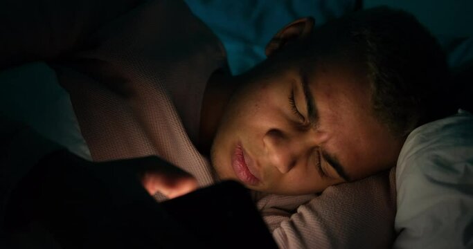 Man waking up and checking his mobile phone late night in bed at home