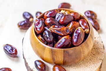 Sweet dried dates in round wooden bowl on light background in the kitchen.