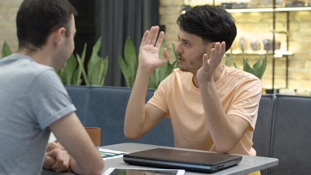Portrait of excited young man talking with friend in cafe. Handsome brunette Caucasian guy meeting mate in coffee house. Male friendship concept. Cinema 4k ProRes HQ.
