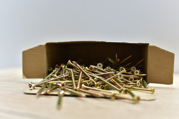 Self-tapping screws in a cardboard box on wooden table. Screw for working with wood products and surfaces. Hardware, fasteners and materials for construction and repair.