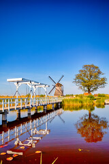 Fototapeta na wymiar Holland Traveling. Traditonal Wooden Dutch Bridge in Kinderdijk Village with Windmill in Background in the Netherlands At Daytime.