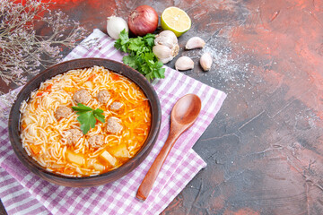Side view of delicious chicken soup with noodles greens and spoon on pink stripped towel oil bottle garlic lemon on dark background