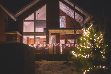 A view of cozy wooden scandinavian cabin cottage chalet house covered in snow near ski resort in winter with the lights on, evening picture