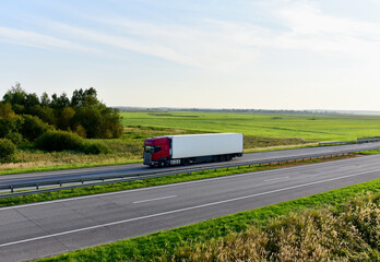 Truck with semi-trailer driving along highway on the sunset background. Goods delivery by roads. Services and Transport logistics. Soft focus.