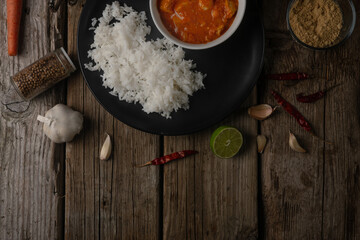 View from above of plate with delicious chicken tikka masala curry and rice on rustic wooden table with spices background. Traditional Indian dish. Exotic tasty meal. Appetizing photo for cookbook.