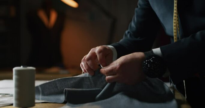 Cinematic shot of experienced tailor is sewing custom handmade high quality apparel in ancient luxury traditional tailoring atelier. Concept of industry, handmade, hand craft, couturier and tradition.