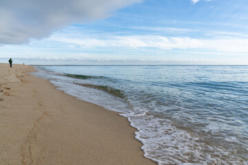 woman walks along an endless golden sand beach with gentle waves